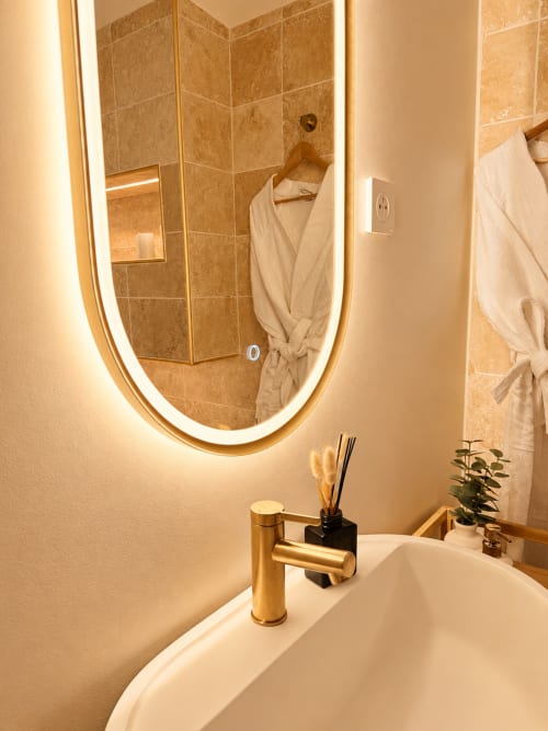 Salle de bains moderne de l'hôtel L'Escapade au Mans avec miroir lumineux, robinetterie dorée et douche à l'italienne