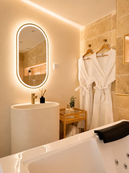 Salle de bain moderne et luxueuse à l'hôtel L'Escapade au Mans avec miroir ovale éclairé, lavabo blanc et peignoirs spa