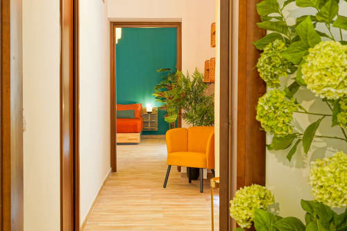 Calaba Decumani apartment hallway with yellow-green plants, orange chair, and colorful teal and orange living space beyond
