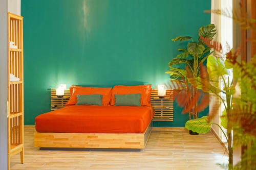 Calaba Decumani apartment bedroom in Naples with orange bedding, teal walls, wooden furniture, and potted plants.