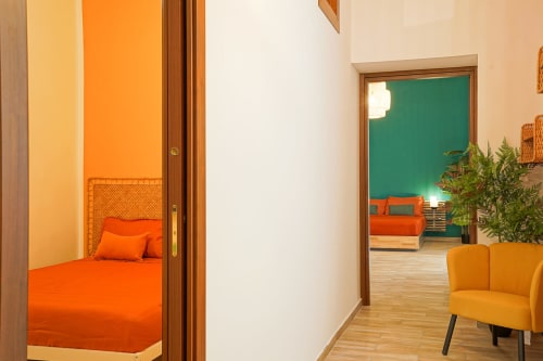 Calaba Decumani apartment in Naples showing bedroom with orange bedding, green accent wall, and yellow armchair in living