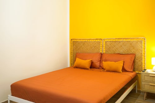 Bright bedroom at Calaba Napoli B&B with orange bedding, woven headboard, and yellow accent wall