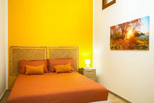 Bright orange bedroom at Calaba B&B in Naples with yellow accent wall, woven headboard, and sunset landscape art