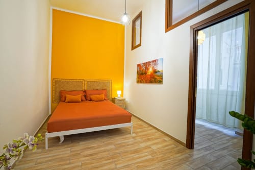Bright bedroom at Calaba Decumani apartment in Naples with orange accents, wooden flooring, and city view access