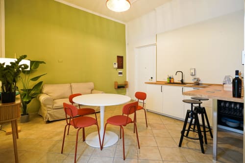 Bright Calaba Decumani apartment in Naples with yellow accent wall, cream sofa, round white dining table, red chairs, and
