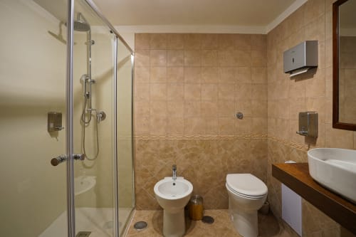 Modern bathroom in Calaba Decumani apartment, Naples, featuring tiled shower, bidet, toilet, and vessel sink with wooden