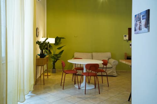 Calaba Decumani apartment in Naples with green walls, white round table, red chairs, and beige sofa