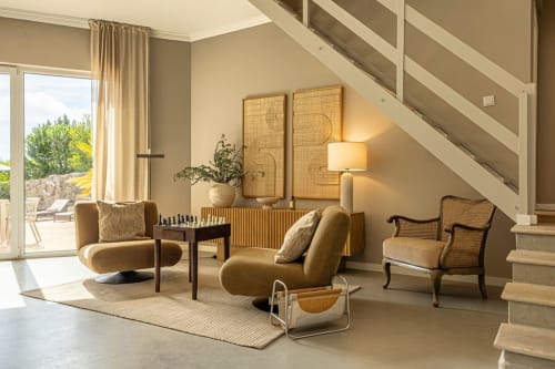 Modern living room at Sea'Ya Villas in Cascais with curved mustard chairs, geometric wall art, and staircase.