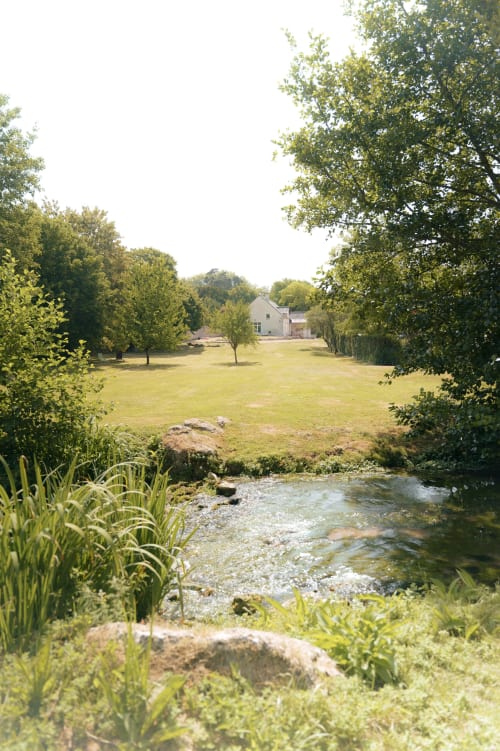 Vue pittoresque du jardin du gîte Le Hameau de Céline avec ruisseau, pelouse soignée et propriété campagnarde