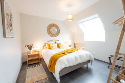 Chambre mansardée lumineuse au Hameau de Céline avec lit blanc, touches jaunes, échelle en bois et puits de lumière.