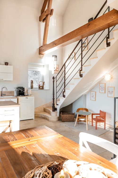 Intérieur de cottage moderne au Hameau de Céline avec escalier à poutres, cuisine ouverte et salle à manger baignée de lumière naturelle