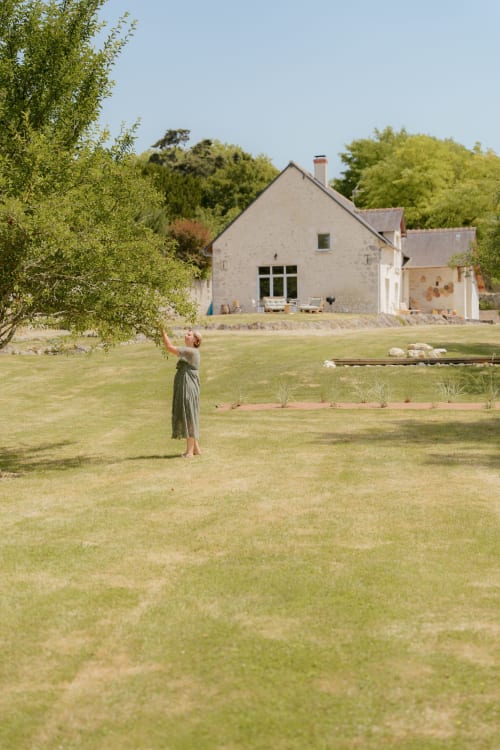 Femme dans le jardin face au cottage en pierre moderne du Hameau de Céline, boutique hôtel de campagne français aux pelouses impeccables