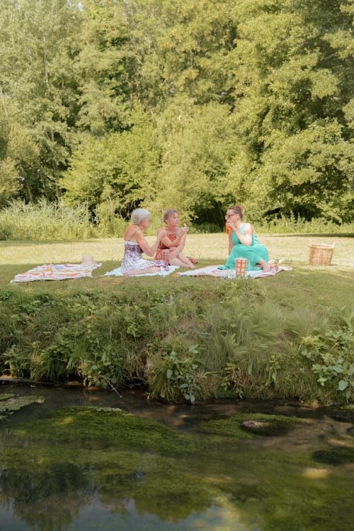 Trois femmes profitant d'un pique-nique au bord de la rivière au jardin Le Hameau de Céline à Landes-le-Gaulois