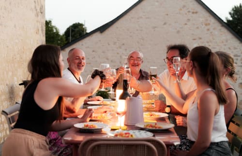 Réunion familiale au Hameau de Célin, verres levés lors d'un dîner en plein air au coucher de soleil avec bâtiments en pierre rustique en arrière-plan