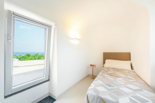 Camera luminosa a Origenes Rooms Procida con letto singolo, vista mare attraverso la porta vetrata e paesaggio costiero