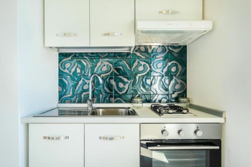 Cucina moderna nell'appartamento Ariè presso Origenes Rooms, Procida con piastrelle azzurre decorate, fornello, lavandino e armadi bianchi