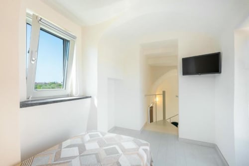 Camera luminosa e moderna alle Origenes Rooms di Procida, con TV schermo piatto, finestra sulla giardino e arredamento minimalista