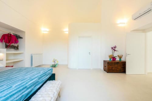 Camera moderna nell'appartamento Ariè di Origenes Rooms, Procida con letto a righe blu, cassettone in legno, porte bianche e luminosa