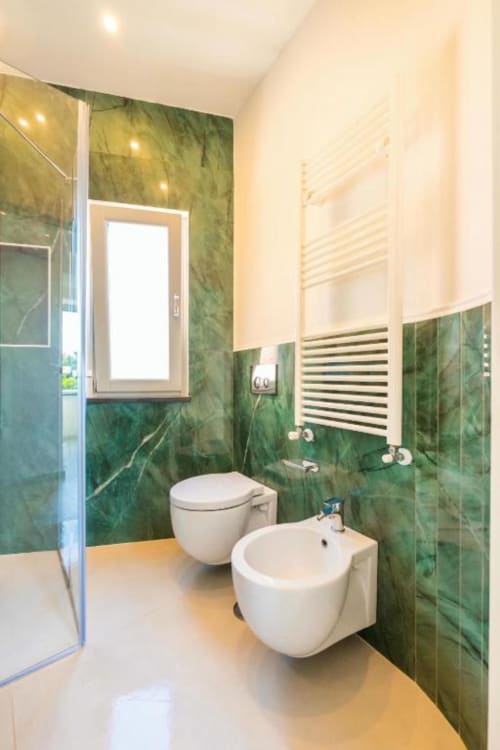 Bagno moderno alle Origenes Rooms a Procida con pareti in marmo verde, wc e bidet bianchi, scaldasalviette e finestra