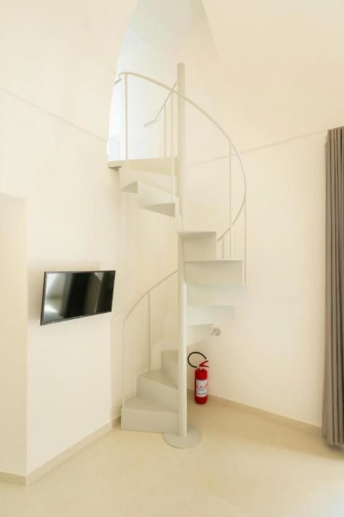 Moderna scala a spirale nell'accogliente appartamento Ariè di Origenes Rooms a Procida, con TV a parete e estintore