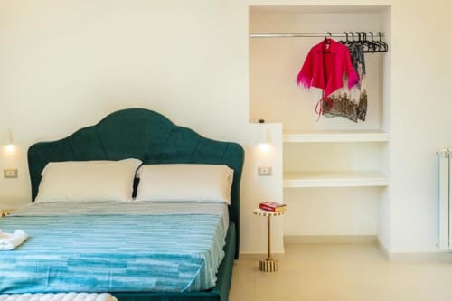 Camera moderna alle Origenes Rooms di Procida con letto dalla testata verde, cuscini color crema, plaid a righe blu e ripiani incorporati