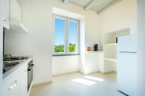 Cucina moderna luminosa nell'appartamento Ariè di Origenes Rooms, Procida con mobili bianchi, elettrodomestici in acciaio inossidabile e
