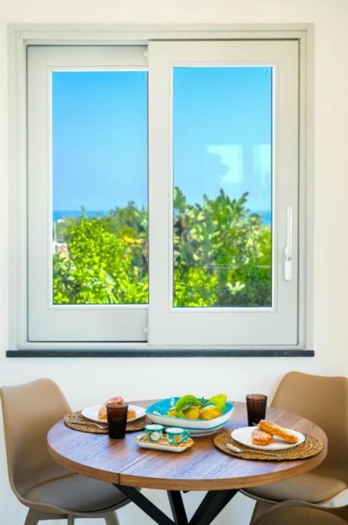 Zona pranzo dell'appartamento Ariè a Procida con vista sul mare e giardino attraverso le porte scorrevoli in vetro