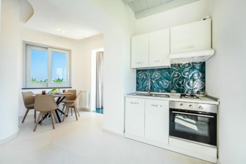 Cucina moderna con mobili bianchi e rivestimento teal a motivi nell'appartamento Ariè presso Origenes Rooms, Procida