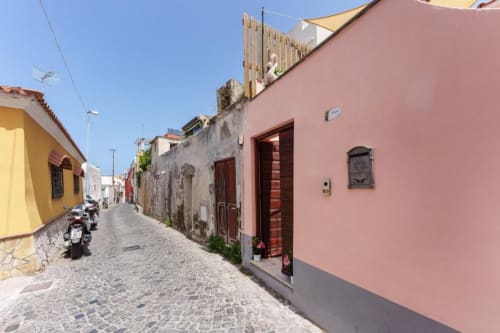 Edifici colorati su una pittoresca via pavimentata a Procida, Italia, dove Origenes Rooms offre appartamenti vacanza.