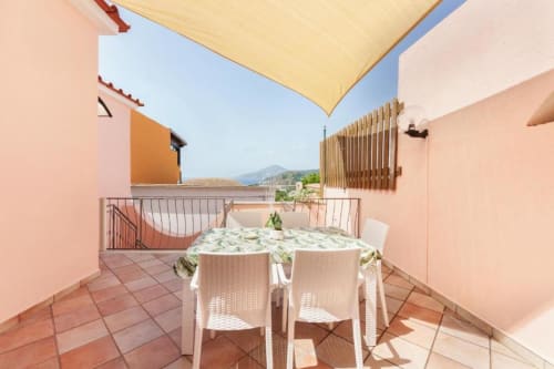 Terrazza soleggiata di Origenes Rooms a Procida con tavolo da pranzo, tenda gialla e vista costiera sull'isola italiana