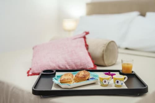 Vassoio con colazione, pasticcini e succo di frutta nel letto della camera Origenes Rooms a Procida, Italia