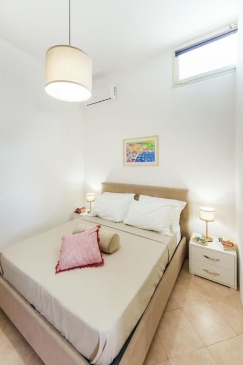 Camera da letto moderna e luminosa agli Origenes Rooms di Procida con letto queen, lampada a sospensione, comodini e finestra con vista sul mare