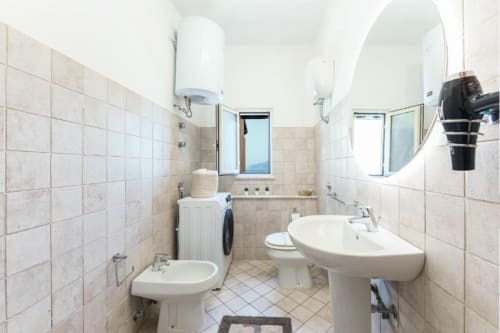 Luminoso bagno con due lavabi su colonna, toilette, bidet e specchi rotondi presso Origenes Rooms a Procida, Italia