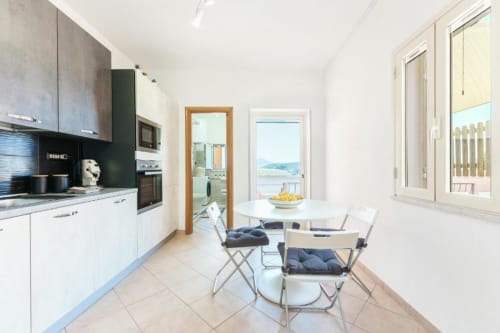 Cucina e zona pranzo moderna con vista sul mare, mobili bianchi, tavolo da pranzo e accesso alla terrazza