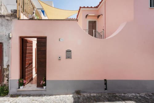 Edificio residenziale con muri rosa presso Origenes Rooms a Procida, Italia, con porta in legno, terrazza e vista sul mare