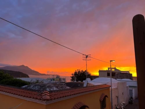 Vista tramonto dalla terrazza di Origenes Rooms a Procida, Italia con oceano e sfondo montuoso