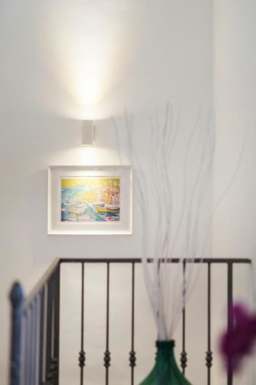 Camera luminosa a Origenes Rooms a Procida con quadri costieri incorniciati sopra il letto in ferro e applique a parete