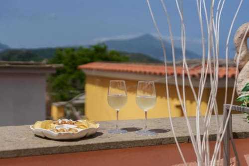 Due calici di vino sulla terrazza di Origenes Rooms a Procida con stuzzichini e vista sul mare delle colorate case