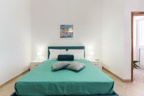 Camera luminosa all'Origenes Rooms di Procida con letto turchese, comodini bianchi e accesso alla terrazza