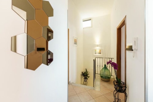 Luminoso corridoio dell'appartamento a Procida con specchi esagonali, pavimento in cotto e fiori in vaso vicino alle porte in legno