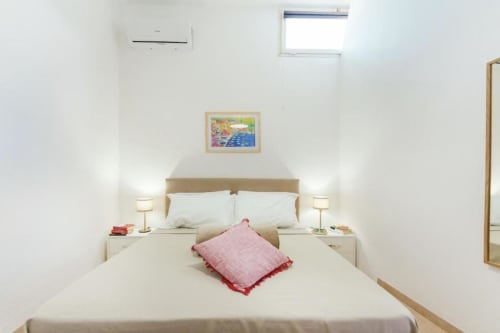 Camera luminosa e minimalista agli Origenes Rooms di Procida con biancheria bianca, cuscino rosa, aria condizionata e arredamento colorato