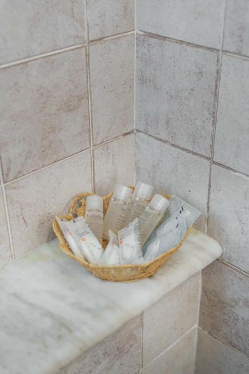 Cesto intrecciato con articoli da bagno su ripiano in marmo nell'angolo del bagno presso Origenes Rooms, Procida