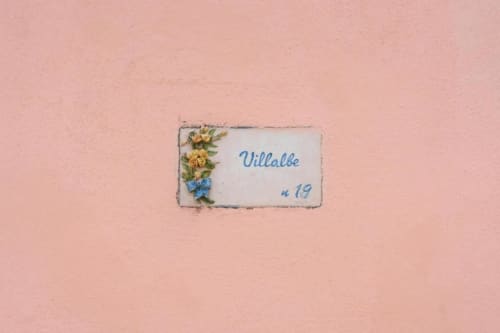 Targa dell'appartamento Villalbe con fiori gialli su muro rosa presso Origenes Rooms a Procida