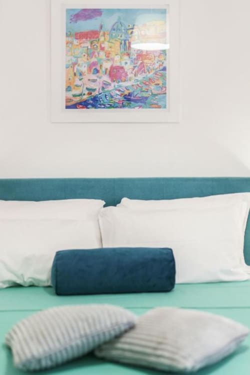 Accogliente camera da letto presso Origenes Rooms a Procida con testata teal, cuscini bianchi e coloratissime opere d'arte costiera sopra il letto