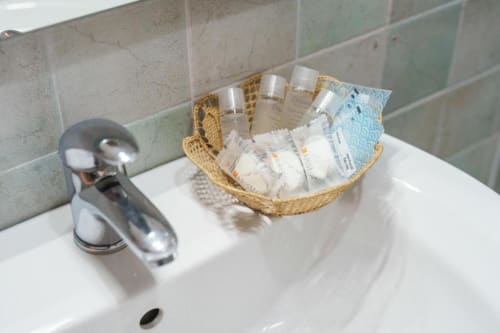 Lavabo della stanza presso Origenes Rooms a Procida con amenities omaggio in cesto intrecciato e rubinetteria cromata