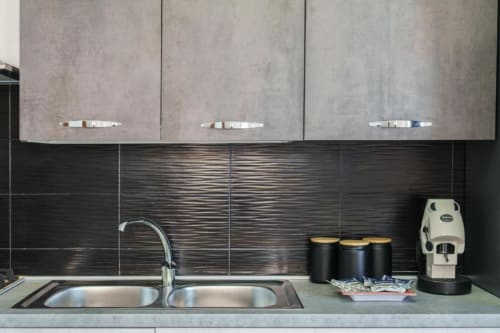 Cucina moderna con doppio lavello in acciaio inox, paraschizzi in piastrelle nere, mobiletti grigi e macchina da caffè nell'appartamento di Procida