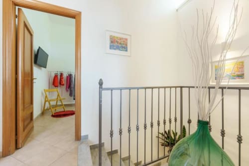 Pianerottolo della scala presso Origenes Rooms a Procida con ringhiera in metallo, pianta verde e accesso alla camera da letto.