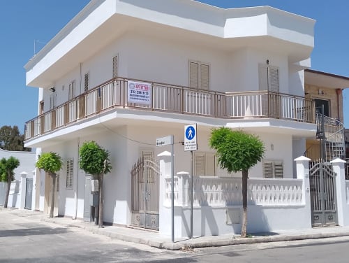 Moderno edificio bianco a Torre Lapillo con balconi, piante verdi e negozi al piano terra