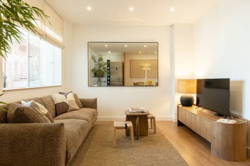 Modern living room at Sea'Ya Villas in Cascais with beige sofa, wooden furniture, and mirrored wall accent
