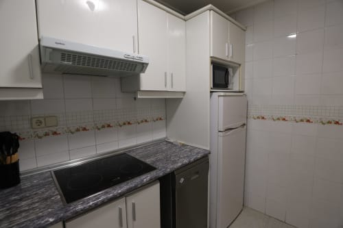 Cocina moderna con armarios blancos, encimera de granito negro, estufa eléctrica y azulejería decorativa en Madrid